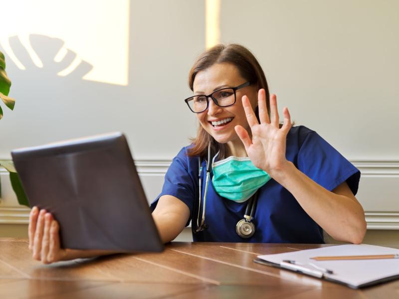 female physician waving and smiling to tablet